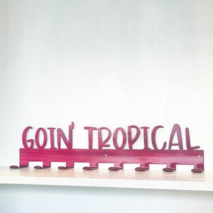 May include: A pink metal coat rack with the words "goin' tropical" in white lettering. The rack has 10 hooks.