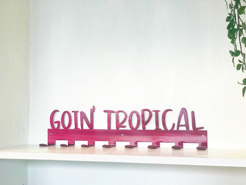 May include: A pink metal coat rack with the words "goin' tropical" in white lettering. The rack has 10 hooks.