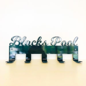 May include: Black metal wall hook with the words "Blacks Pool" in a decorative font. The hook has five hooks for hanging items.