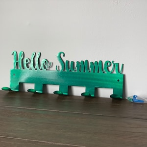 May include: Green metal wall hook with the words "Hello Summer" cut out. The hook has six hooks for hanging items.