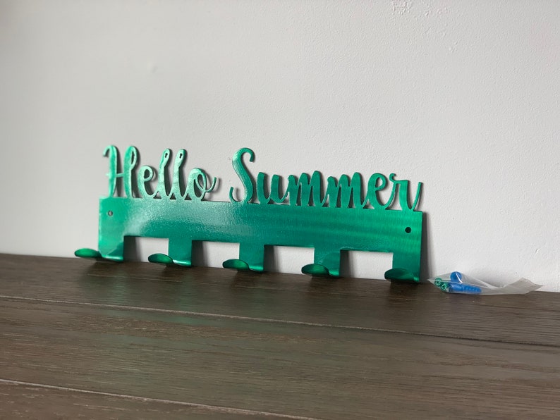 May include: Green metal wall hook with the words "Hello Summer" cut out. The hook has six hooks for hanging items.