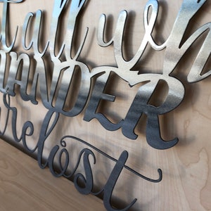 May include: Metal wall art with the quote "Not all who wander are lost". The art is made of brushed metal and has a modern, minimalist style.