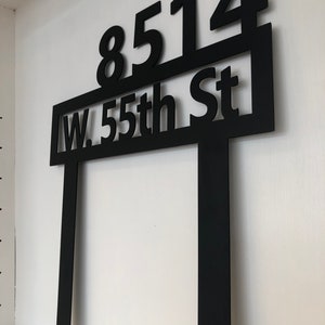 May include: Black metal yard sign with the address "8514 W. 55th St" in white lettering.
