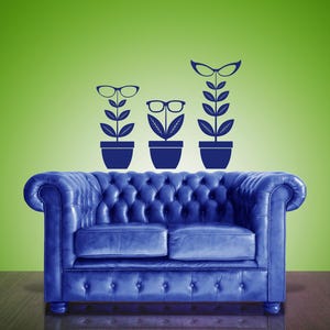 Puede incluir: Un sofá Chesterfield de cuero azul con un diseño capitoné. Encima del sofá, tres plantas en macetas con gafas como flores se representan sobre un fondo verde. El sofá está sobre un suelo de madera oscura.