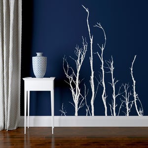 May include: A white side table with a blue and white patterned vase on top. A navy blue wall features a white tree branch design. A white curtain is on the left side of the image.