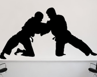 May include: Silhouette of two people in a martial arts pose, one kneeling and the other standing with a leg extended. The silhouettes are black against a white background.