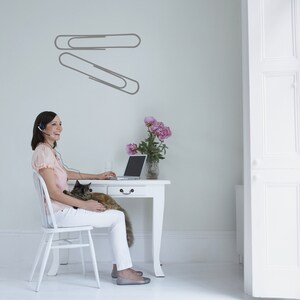 Stationery wall decal with oversized paper clip illustration, contemporary office art for corporate decor, classroom walls, and reflective historical symbolism.