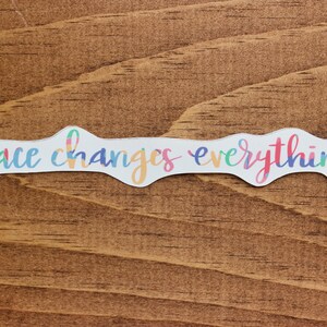 May include: A white sticker with a colorful, wavy, handwritten font that reads "grace changes everything".