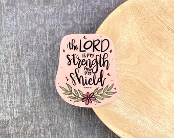 May include: Pink and green floral design with the text "The Lord is my strength and my shield" and the scripture reference "Psalm 28:7".