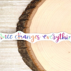May include: A colorful sticker with the text "grace changes everything" on a wooden background.