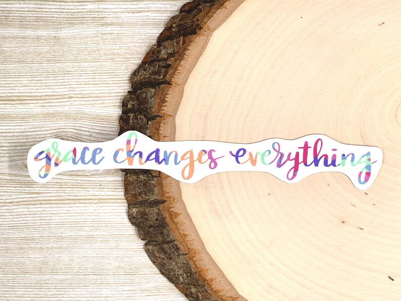 May include: A colorful sticker with the text "grace changes everything" on a wooden background.
