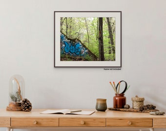 May include: Framed art print featuring a vibrant scene of graffiti art on a concrete structure, set against a backdrop of lush green trees. The artwork is displayed on a light-colored wall above a wooden desk with decorative items.