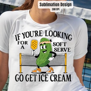 May include: White t-shirt with a green pickle character holding a yellow paddle and the text "If you're looking for a soft serve, go get ice cream".