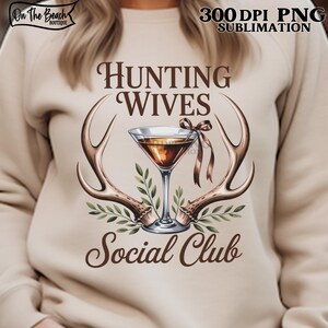 May include: A beige sweatshirt with the text "Hunting Wives Social Club" in brown script. The design includes a martini glass, antlers, and greenery. The top right corner has the text "300 DPI PNG SUBMLIMATION". The top left corner has the text "On The Beach Boutique".