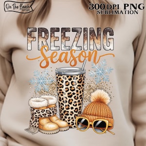 Puede incluir: Camiseta gráfica beige con las palabras "FREEZING Season" en marrón y naranja. El diseño incluye un vaso con estampado de leopardo, botas de invierno, un gorro de punto, gafas de sol y copos de nieve. La imagen está etiquetada como "300 DPI PNG SUBLIMATION".