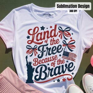 May include: White t-shirt with a patriotic design. The design includes the text "Land of the Free Because of the Brave" in red and navy blue, along with an American flag, stars, and the Statue of Liberty.