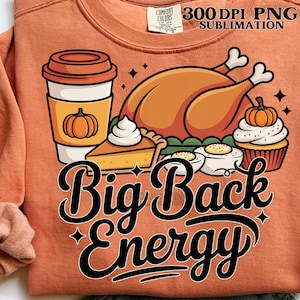 May include: Orange sweatshirt with a Thanksgiving-themed graphic. The design includes a coffee cup with a pumpkin, a roasted turkey, pie, cupcakes, and the text "Big Back Energy". The sweatshirt has a crew neck and long sleeves.