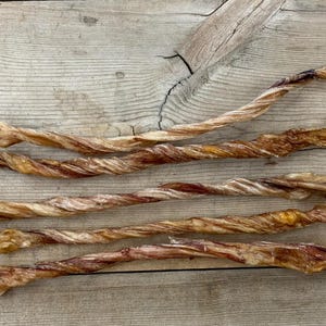 May include: Five twisted, dried beef bully sticks on a wooden surface. The sticks are light brown and have a slightly reddish hue.