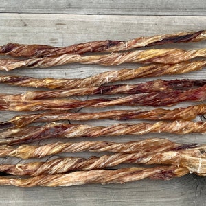 May include: A close-up of a pile of twisted, dried beef bully sticks. The sticks are a light brown colour and have a slightly reddish hue. They are arranged in a random pattern on a wooden surface.