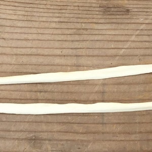 May include: Two long, thin, white bones lying parallel to each other on a brown wooden surface.
