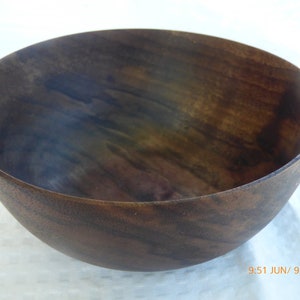 May include: A large, dark brown wooden bowl with a smooth, polished finish. The bowl has a wide, rounded base and a slightly flared rim.