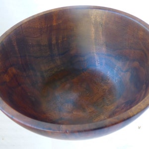 May include: A large, dark brown wooden bowl with a smooth, polished finish. The bowl is empty and has a slight curve to the sides.