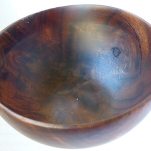 May include: A dark brown wooden bowl with a smooth, polished finish. The bowl is empty and has a slight curve to the sides.