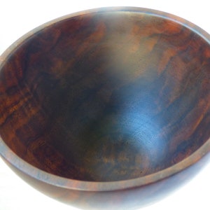 May include: A large, dark brown wooden bowl with a smooth, polished finish. The bowl is empty and has a slight curve to the sides.
