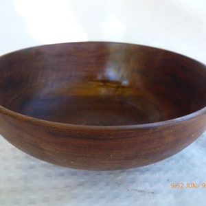 May include: A large, dark brown wooden bowl. The bowl is made of a single piece of wood and has a smooth, polished finish.