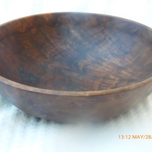 May include: A large, dark brown wooden bowl with a smooth, rounded surface. The bowl is made of a single piece of wood and has a natural, rustic look.