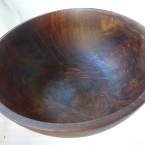 May include: A large, dark brown wooden bowl with a smooth, polished finish. The bowl is empty and has a slight curve to the sides.