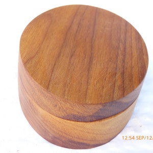 May include: A round, wooden box with a lid. The box is made of a light brown wood with visible grain patterns. The box is cylindrical in shape and appears to be handcrafted. The image includes the date and time stamp.