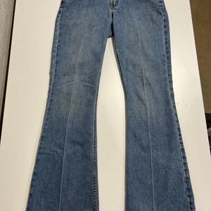 May include: Light blue denim jeans with a low-rise waist and flared legs. The jeans feature a classic five-pocket design, belt loops, and a button and zip closure. The denim has a faded wash and subtle wear marks.