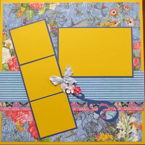 May include: A scrapbook page with a floral and butterfly theme. It features yellow photo mats with blue borders, a blue and white striped accent, and decorative butterflies and flowers. The background has a floral and insect pattern.