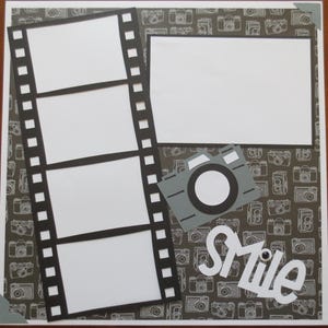 May include: A scrapbook page with a photography theme. It features a film strip design with four photo spaces, a rectangular photo space, and a gray camera cutout. The background is patterned with camera illustrations, and the word "Smile" is written in white.