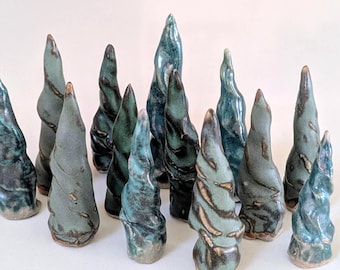May include: A collection of thirteen ceramic sculptures shaped like twisted, conical trees. Each piece features a glossy glaze in varying shades of teal, sage green, and dark charcoal, with textured, spiraling surfaces and pointed tops.