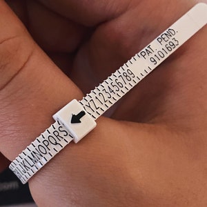 May include: White plastic ring sizer with black markings, including letters from K to S and numbers from 1 to 9. The sizer has an arrow pointing to the right and the text "PAT. PEND. 9101693".