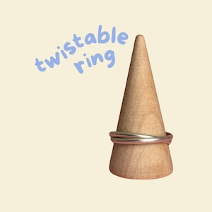 May include: A silver twistable ring on a wooden ring holder. The text "twistable ring" is written in blue above the ring.