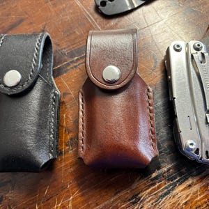 May include: Three leather cases for multi-tools. The cases are brown, black, and brown. The cases have a snap closure and are made of a high-quality leather.