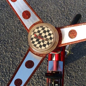 May include: A red and silver toy car with a checkered flag design on the front. The car has a steering wheel and three red and white stripes on the sides.