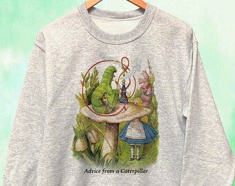 May include: A light gray sweatshirt featuring a colorful illustration from Alice in Wonderland. The graphic depicts a green caterpillar on a mushroom, with Alice and the text "Advice from a Caterpillar". The sweatshirt is hanging on a wooden hanger.