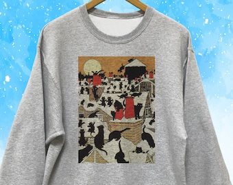Puede incluir: Sudadera gris claro con un estampado gráfico de gatos negros en tejados bajo la luna llena en una escena invernal. El gráfico tiene chimeneas rojas y un fondo marrón y beige.