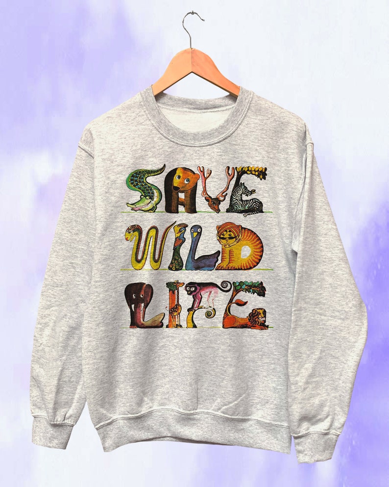 May include: A heather gray sweatshirt with the words "SAVE WILD LIFE" in colorful, animal-shaped letters. The design includes a crocodile, bear, deer, zebra, snake, bird, tiger, elephant, monkey, and lion. The sweatshirt is hanging on a wooden hanger.
