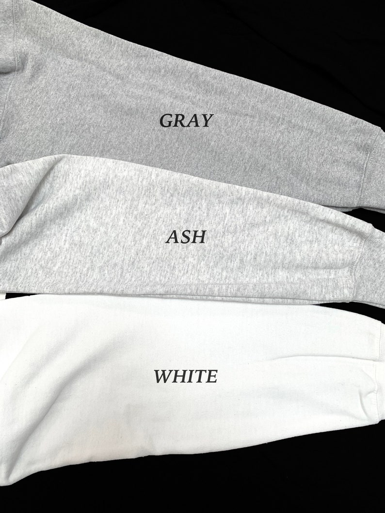 May include: Close-up of three long-sleeved shirts in gray, ash, and white. The word "GRAY" is printed on the gray shirt, "ASH" on the ash shirt, and "WHITE" on the white shirt. The shirts are made of a soft, comfortable material.