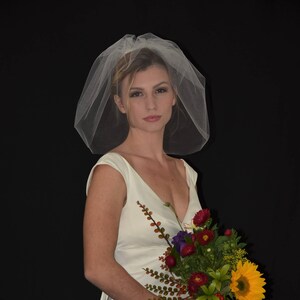 Op de afbeelding: Een bruid in een witte trouwjurk en een witte sluier houdt een boeket bloemen vast. Het boeket bevat zonnebloemen, rode en paarse bloemen en groen blad.