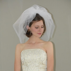 Op de afbeelding: Een bruid in een witte strapless bruidsjurk met delicate borduursels en een witte sluier. Ze houdt een boeket blauwe en groene hortensia's vast.