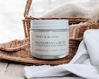 May include: A glass jar of Poppy & Bloom Deodorant Cream with a white lid. The label reads "Aluminum & Baking Soda Free" and "Grapefruit Lemon". The jar is 2.5 oz and sits near a woven basket and white cloth.