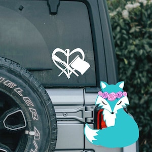 May include: A silver SUV with a black spare tire and a blue fox sticker on the back window. The fox is wearing a pink flower crown.