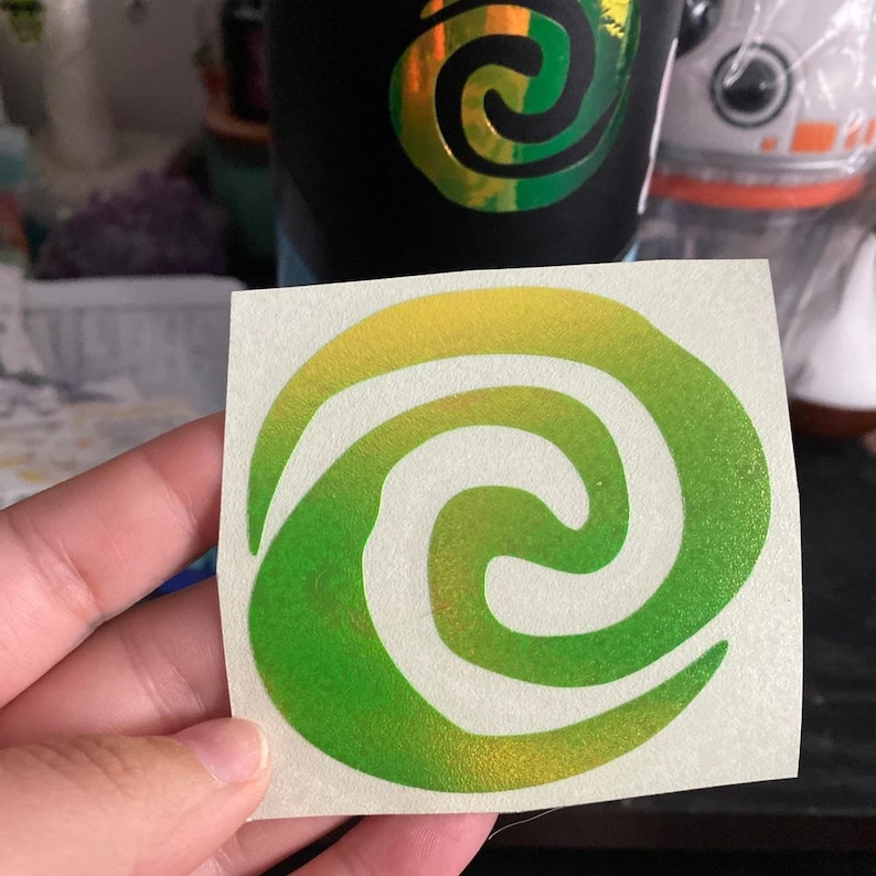 May include: A green and yellow iridescent sticker with a white spiral design. The sticker is a popular symbol from the Disney Pixar movie Up.