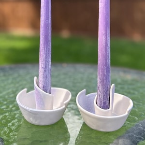 Könnte beinhalten: Zwei weiße Kerzenhalter aus Keramik mit einem einzigartigen Design, die jeweils eine lavendelfarbene Kerze halten.